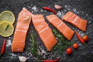 Raw salmon filet with herbs and spices on dark black background Fresh salmon fish for cooking salad or steak seafood pepper rosemary lemon pepper photo