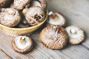 champiñones frescos en la cesta y fondo de mesa de madera - champiñones shiitake foto