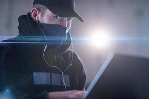 young talented hacker using laptop computer while working in dark office photo