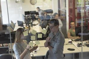 pareja joven en el interior de la oficina moderna escribiendo notas en pegatinas foto