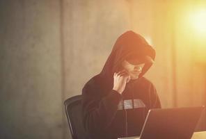 young talented hacker using laptop computer while working in dark office photo