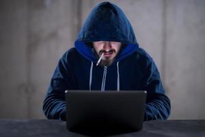 young hacker using laptop computer while working in dark office photo