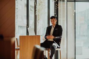 hombre de negocios feliz sentado en la cafetería con laptop y teléfono inteligente foto