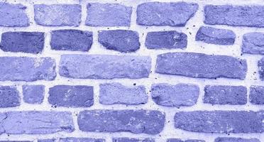 Old brick wall in medieval monastery repainted in trendy very peri color of the year 2022. Rough texture. Horizontal violet stone background with place for text.