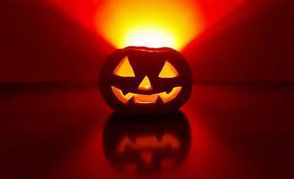 Carved glowing pumpkin with candle inside in dark night and blurred defocused background. The back wall highlighted in yellow red gradient triangle over pumpkin. Halloween traditional jack-o-lantern. photo