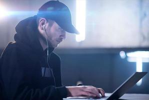young talented hacker using laptop computer while working in dark office photo