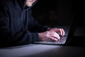 hacker using laptop computer while working in dark office photo
