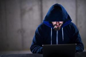 young hacker using laptop computer while working in dark office photo