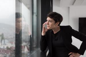 mujer elegante usando teléfono móvil por ventana en edificio de oficinas foto