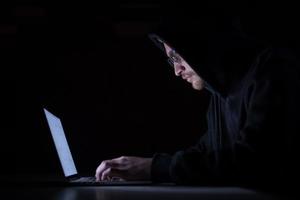 hacker using laptop computer while working in dark office photo