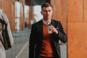 Portrait of tourist man carrying suitcase and holding a cup of coffee while walking outdoors on the street. photo