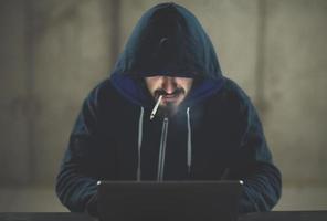 young hacker using laptop computer while working in dark office photo