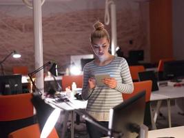 mujer que trabaja en una tableta digital en la oficina nocturna foto