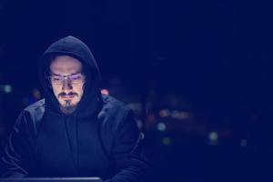 hacker using laptop computer while working in dark office photo