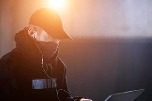 young talented hacker using laptop computer while working in dark office photo