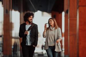 two young people on a break from work walk in front of a modern company where they work and drink coffee. photo