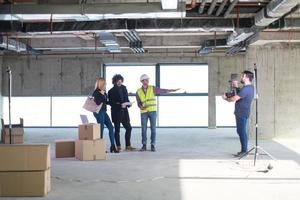 videographer recording while architect showing house design plans to a young couple photo