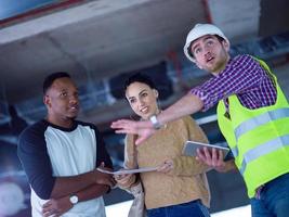 worker showing house design plans to a young multiethnic couple photo