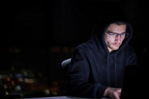 hacker using laptop computer while working in dark office photo