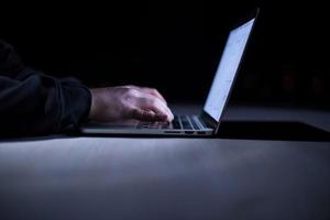 hacker using laptop computer while working in dark office photo