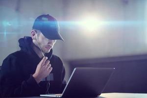 young talented hacker using laptop computer while working in dark office photo