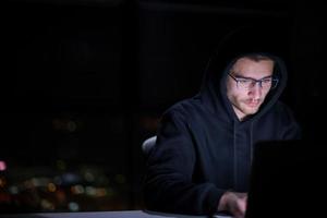 hacker using laptop computer while working in dark office photo