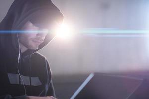 young talented hacker using laptop computer while working in dark office photo