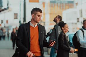 ir a la terminal del aeropuerto. viajero de negocios confiado caminando por las calles de la ciudad y tirando de su maleta bebiendo café y hablando en el teléfono inteligente foto