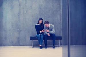 pareja de negocios usando teléfono móvil mientras está sentado en el banco foto