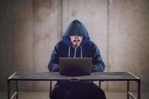 young hacker using laptop computer while working in dark office photo