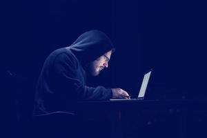 hacker using laptop computer while working in dark office photo