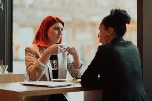 Two young business women sitting at table in cafe.Girl using laptop, smartphone, blogging. Teamwork, business meeting. Freelancers working... photo