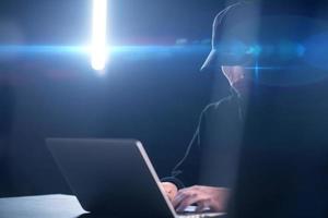 young talented hacker using laptop computer while working in dark office photo