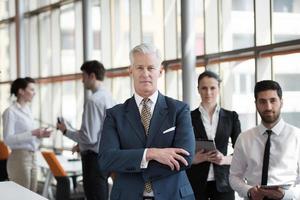 portrait of senior businessman as leader  with group of people in background as team photo