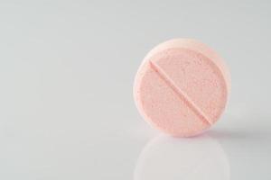 un primer plano de una píldora de vitamina rosa sobre una superficie reflectante blanca. foto