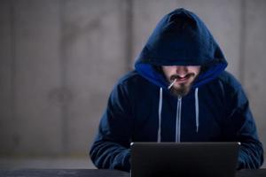 young hacker using laptop computer while working in dark office photo