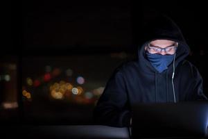 hacker using laptop computer while working in dark office photo