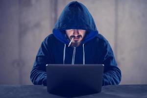 young hacker using laptop computer while working in dark office photo