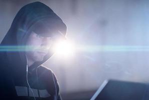 young talented hacker using laptop computer while working in dark office photo