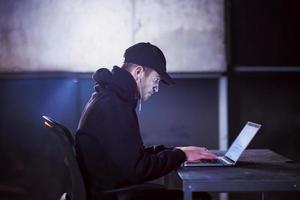 talented hacker using laptop computer while working in dark office photo