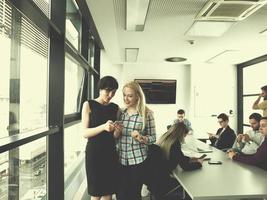 dos mujeres elegantes usando teléfono móvil por ventana en edificio de oficinas foto