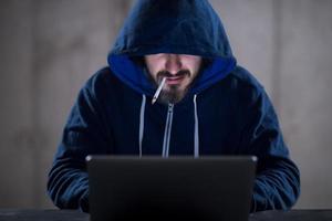 joven hacker que usa una computadora portátil mientras trabaja en una oficina oscura foto