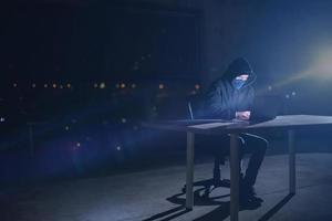 hacker using laptop computer while working in dark office photo