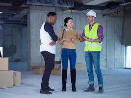 worker showing house design plans to a young multiethnic couple photo