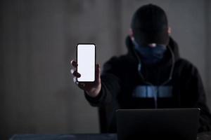 criminal hacker using laptop computer while working in dark office photo