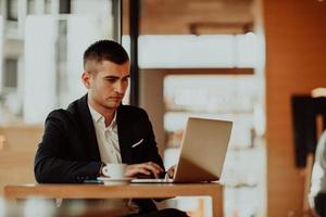 hombre de negocios feliz sentado en la cafetería con laptop y teléfono inteligente foto