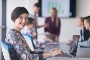 mujer de negocios joven en la oficina que trabaja en la computadora portátil con el equipo en la reunión en segundo plano foto