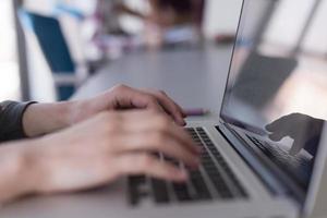 close up of business womans hand typing on laptop with team on meeting in background photo