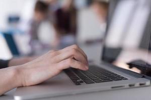 close up of business womans hand typing on laptop with team on meeting in background photo