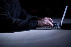 hacker using laptop computer while working in dark office photo